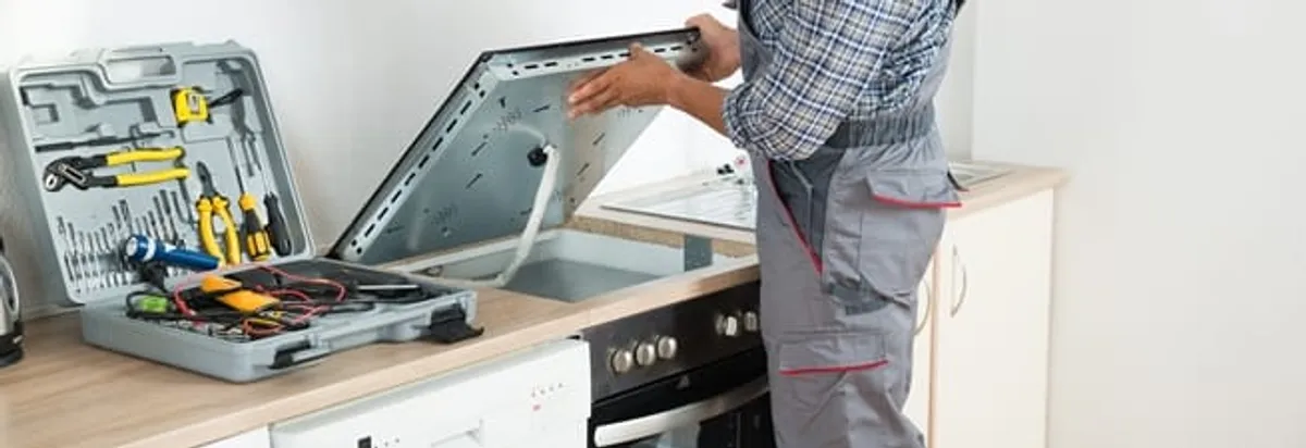 Cooktop repair technician lifting a built-in stovetop for service in Dover, DE