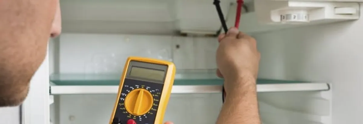 Refrigerator repair technician testing electrical components with a multimeter in Dover, DE