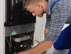 Refrigerator repair technician servicing the compressor and condenser area in Dover, DE
